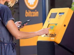 A person holds a phone while tapping a screen on an orange Bitcoin ATM