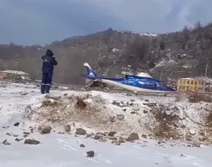 A man in blue snow gear stands next to a blue helicopter in a snowy region