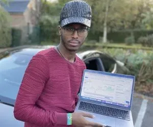 Photograph of a man holding a laptop while standing in front of a Mercedes