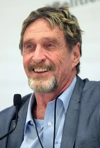 Portrait of John McAfee, speaking at a microphone