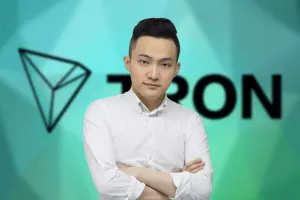 Justin Sun stands with his arms crossed in front of a green and blue background with the Tron logo