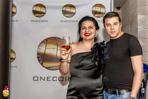 Ruja Ignatova and Karl Sebastian Greenwood photographed in front of a OneCoin branded backdrop