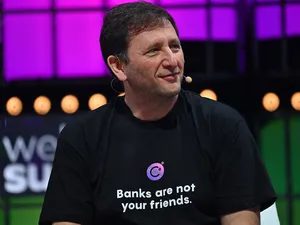 Alex Mashinsky sitting onstage, wearing a Madonna microphone and a t-shirt reading "Banks are not your friends." with the Celsius logo