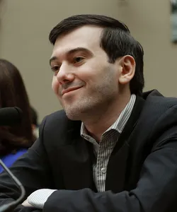 Martin Shkreli sits at a table, arms crossed and smirking