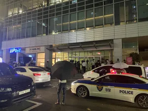 Korean police cars parked outside an office building at nighttime. A lit "Upbit" sign is visible.